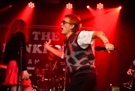 A male singer on a stage wearing sunglasses, holding a microphone, dancing