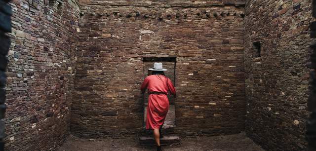 a person in a red dress enters a weathered stone doorway inside a stone room
