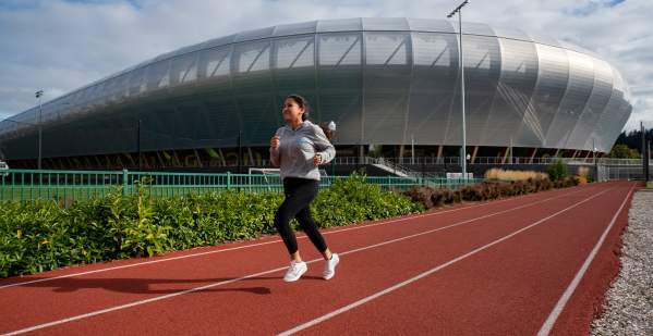 A woman running on a track surface in front of Hayward Field.