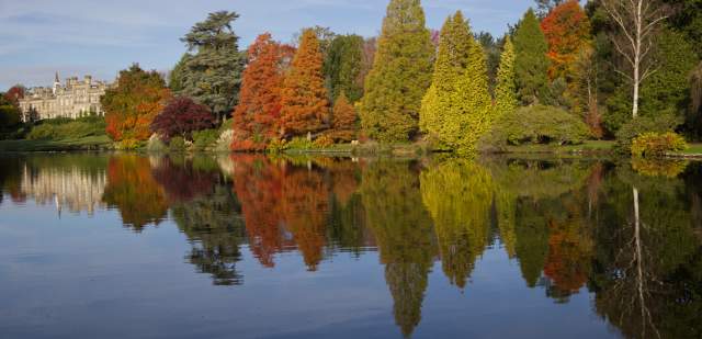 Sheffield Park house in distance with autumnal trees alongside the lake