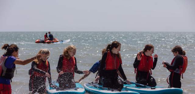 A group of young people wearing red life vests sit on paddleboards in the sea at Eastbourne