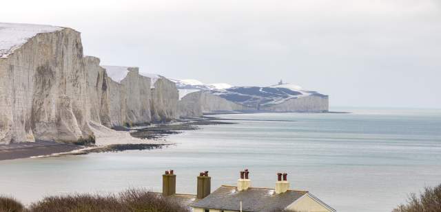 seven sisters in the snow during winter. the cliffs are in the distance with some cottages in the foregorund.