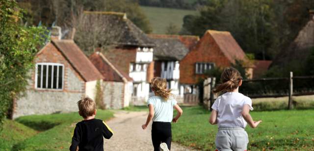 Three children run along the path towards the old buildings at Weald and Downland museum, Sussex