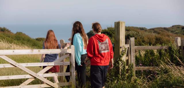 A group of 3 young people walking through a gate towards the sea on the Sussex Downs
