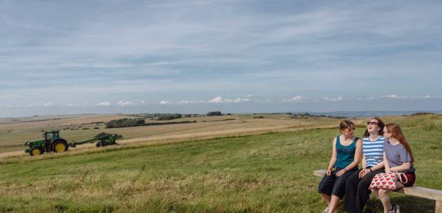 Group of girls sitting on top of the Downs with a tractor ploughing the fields
