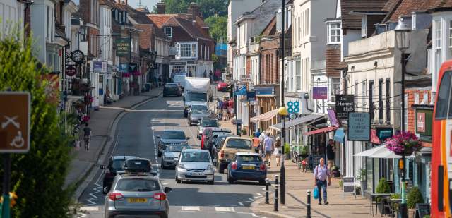 A busy high street with traffic in the historic town of Battle, Sussex, with shop fronts and shoppers