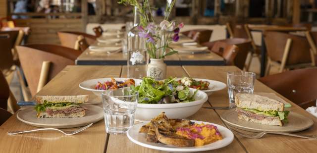 A wooden table set for lunch with plated food and glassware, at Knepp kitchen in Sussex