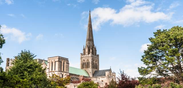 A view of Chichester Cathedral from the gardens with the spire reaching blue sky