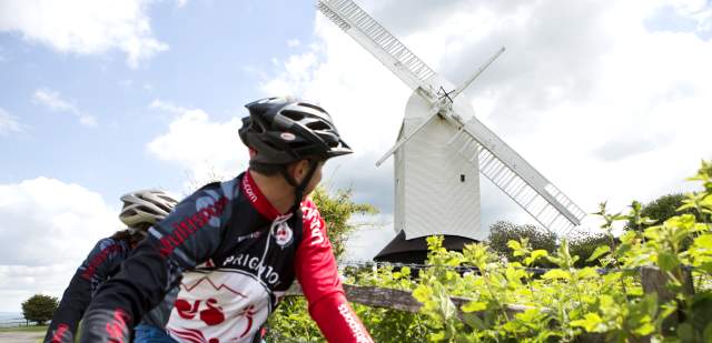 Two mountain bikers ride past a white wooden windmill in the South Downs National Park