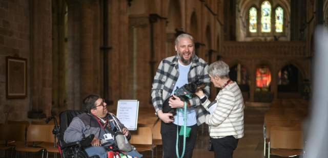 Wheelchair user with friends holding their dog, standing in Chichester Cathedral