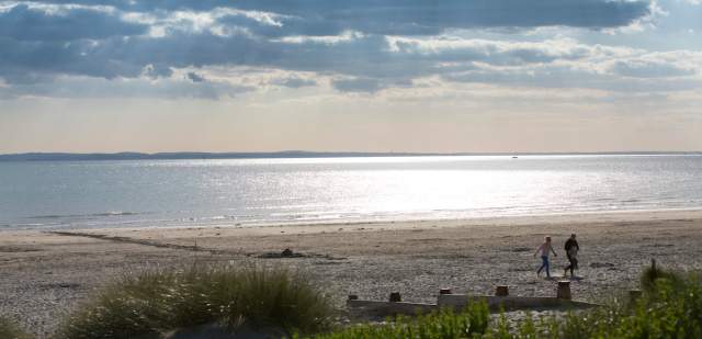 Sunny day at West Wittering beach looking out to sea, with a couple walking in the sandy dunes