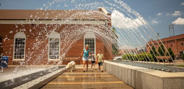 Family and dog walking under water feature in Downtown Kannapolis