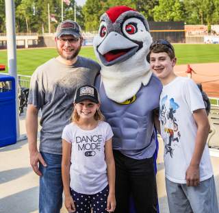 Family posing with a baseball team mascot at a stadium, smiling during a game-day event