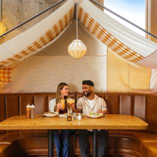 Young Couple sitting and holding drinks in a booth with a tent canopy overhead, at Union Rec