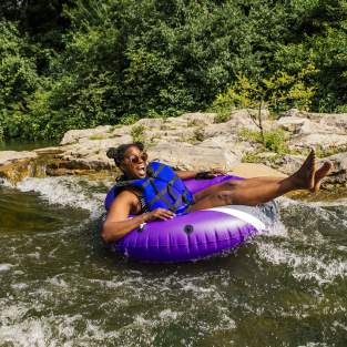 Woman in blue life jacket floating down the Huron River in a purple inner tube