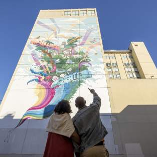 Couple pointing upward at tall, colorful mural