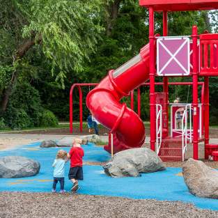 Two small children holding hands walking towards large red play structure