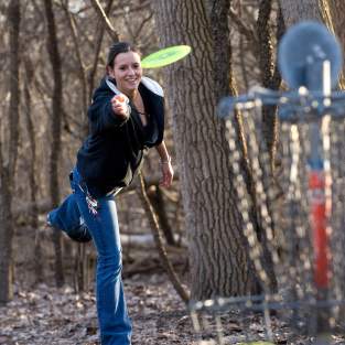 Woman throwing a bright green frisbee at a goal in the foreground