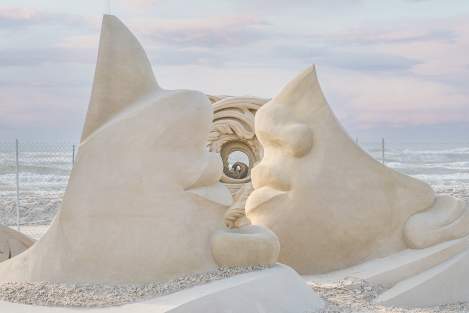 Sand sculpture showing three sculptures. Two are upside down faces.
