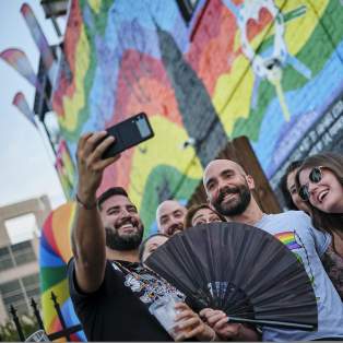 group of people taking a selfie in front of a rainbow mural