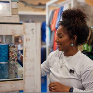woman in long sleeve white shirt reaching for multi-color cups on shelf.