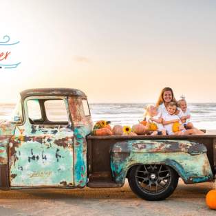 An old truck sits on the beach surrounded by pumpkins. A family sits in the bed of the truck and a logo overlaid on the photo reads "Beachtober."