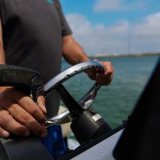 A close up of two weathered hands driving a boat