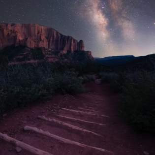Starry Skies over a dirt hiking trail with logs laid out for steps and towering crimson cliffs in the background in Kolob Canyons, Ut.