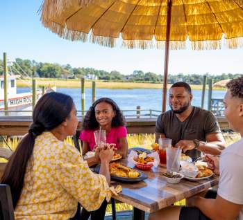 a family of four eating on an outside patio with a view of a shrimp boat and river in the background