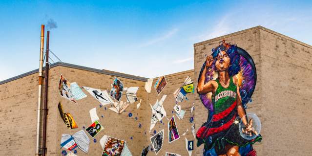 Mural depicting child wearing a dress reading Roxbury blowing bubbles and surrounded by blowing posters and books
