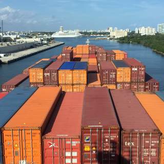 Containers stacked on the deck of an outbound cargo ship.