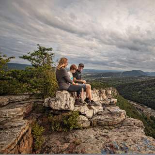 A mom, dad and son sit on a shale cliff overlooking a mountain vista.