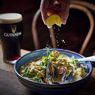 Lemon being squeezed over Seafood Chowder with a pint of Guinness int he background