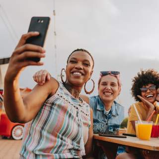 A group of people pose for a selfie while enjoying drinks in an outdoor space.