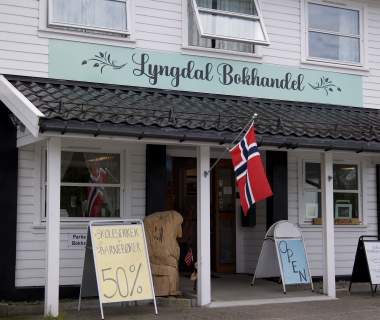 Inngangspartiet til Lyngdal Bokhandel med norsk flagg og tilbudsskilt.