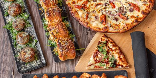 An image of chicken wings, pizza, pizza rolls, and other appetizers spread across a table showcasing the menu at doc & bubbas