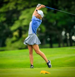 lady golfer in grey skirt and grey and royal blue shirt, white hat.full swing of club