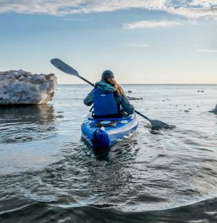 woman kayaks away from photographer between ice formations on Lake Michigan