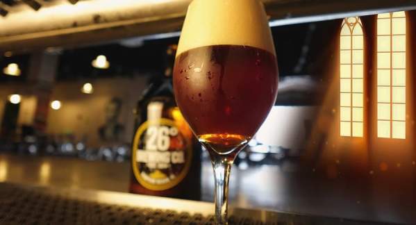 A glass of stout beer sitting on a bar with blurred out taps behind it.