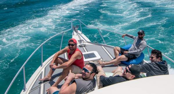 Five guys sitting on the bow of a fishing boat heading out to go fishing in beautifully clear blue waters off Pompano Beach.