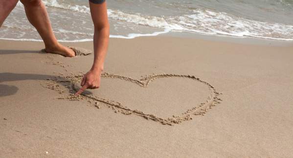 Someone drawing a heart in the sand on a beach