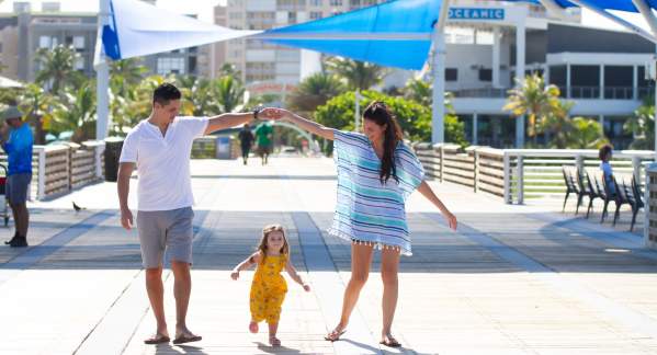 a dad and mom making a hand bridge over their young daughter as they walk on the Pompano Beach Pier