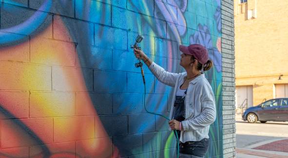 Artist Mindy Allen painting her mural titled Stop and smell the flowers as part of the BOOM! Salina mural festival