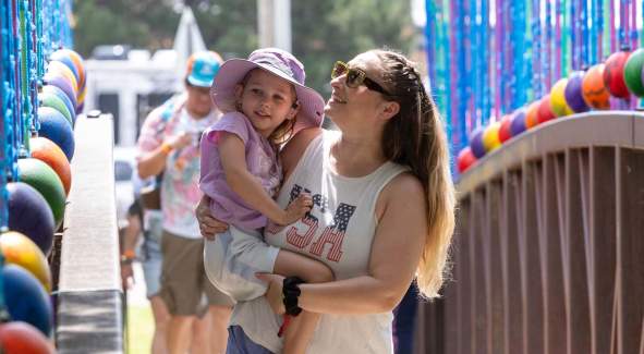 A mom and their kid crossing a colorful bridge at Smoky Hill River Festival in Salina, Kansas.