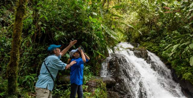 Couple birdwatching, on a green trail, waterfall in the back
