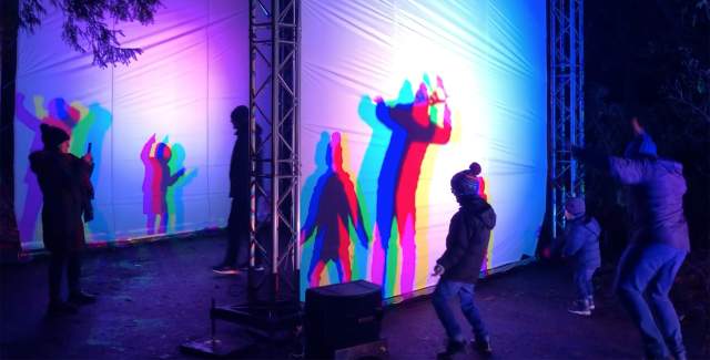 people stood infront of a white screen with shadows projected onto it, in the dark