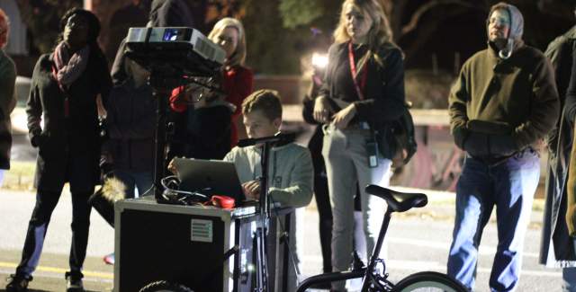 A boy in the street interacting with a computer display with people around him