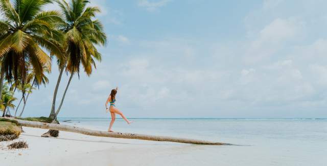 Mujer caminando sobre el tronco de una palmera en la playa de San Blas, Guna Yala en Panamá.