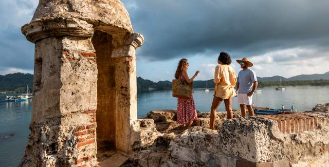 A group admire the ruins of Batería Santiago, at background you can see the coast and beach of Portobelo