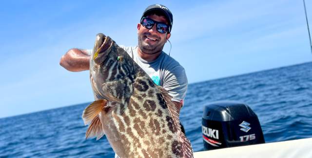 A fisherman showing a huge fish on a boat